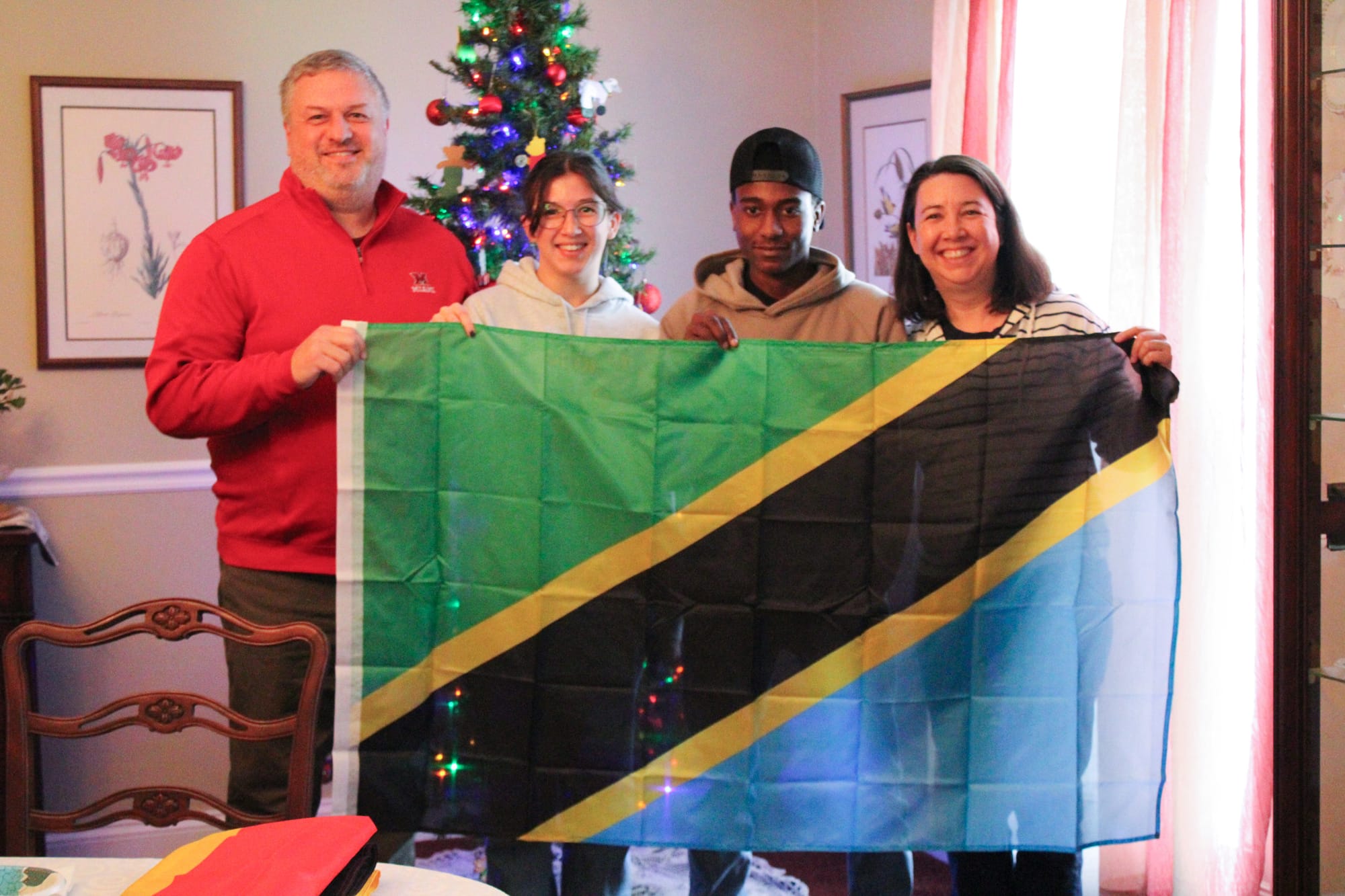 Arkam Nassor, 16, of Tanzania, middle right, poses with his nation’s flag at a lunch for Oxford exchange students alongside his host family, the Greenes.