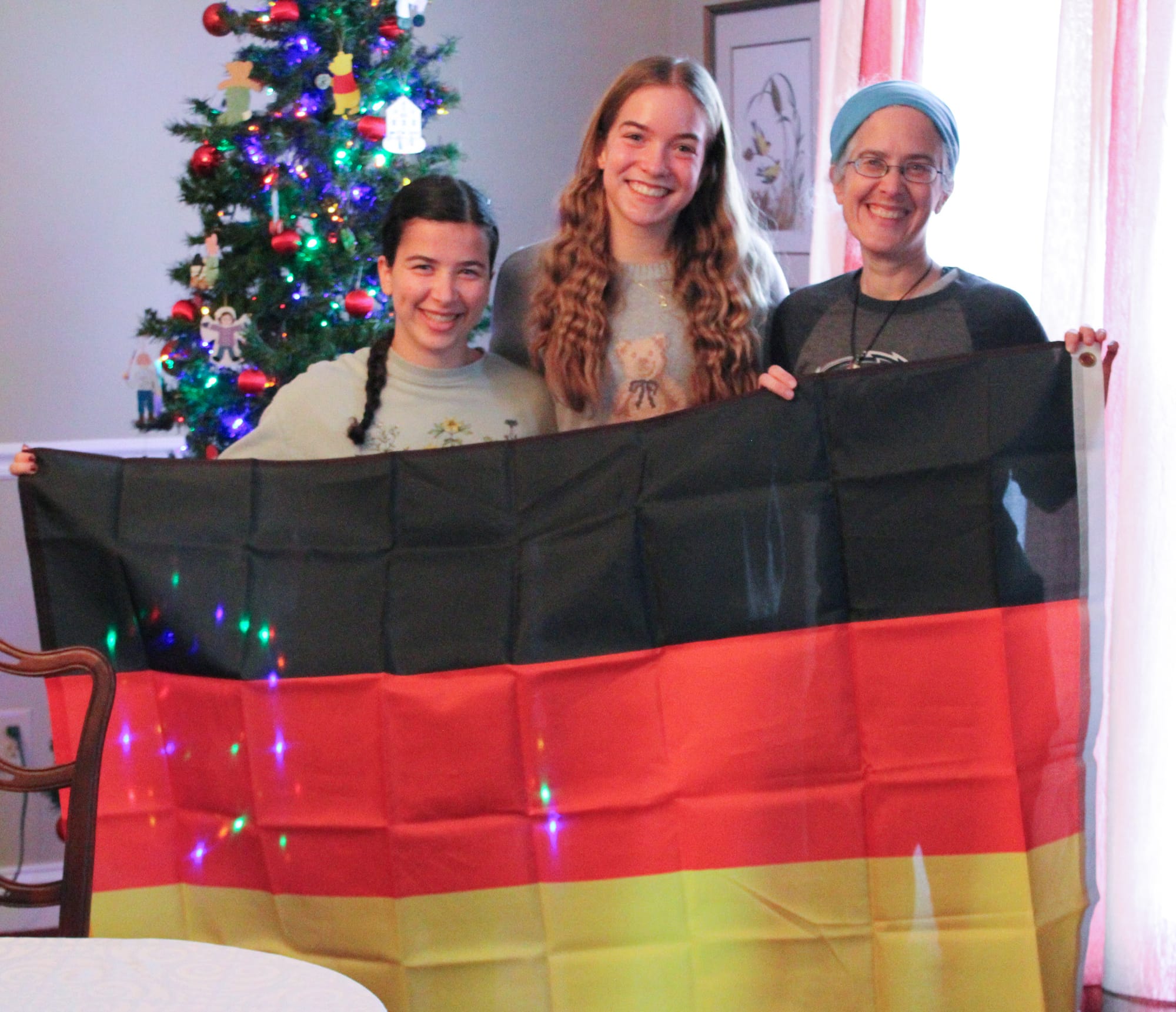 Fee Mayer, 15, of Germany, middle, poses with her nation’s flag at a lunch for Oxford exchange students alongside her host family, Rachel and Leah Wasburn-Moses.