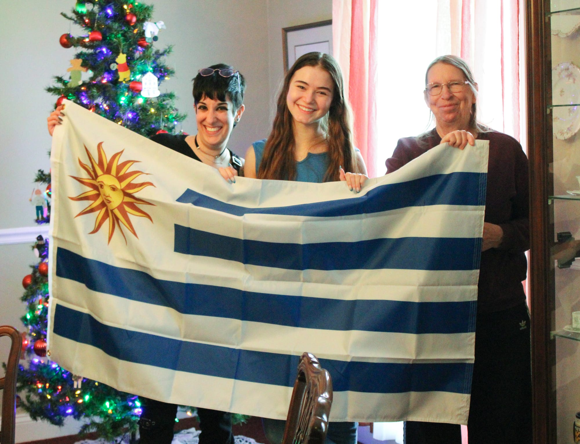 Sofía Charbonnier Fernández, 18, of Uruguay, middle, poses with her nation’s flag at a lunch for Oxford exchange students alongside her host family, Rae Rozman and Sandra McSpadden. 