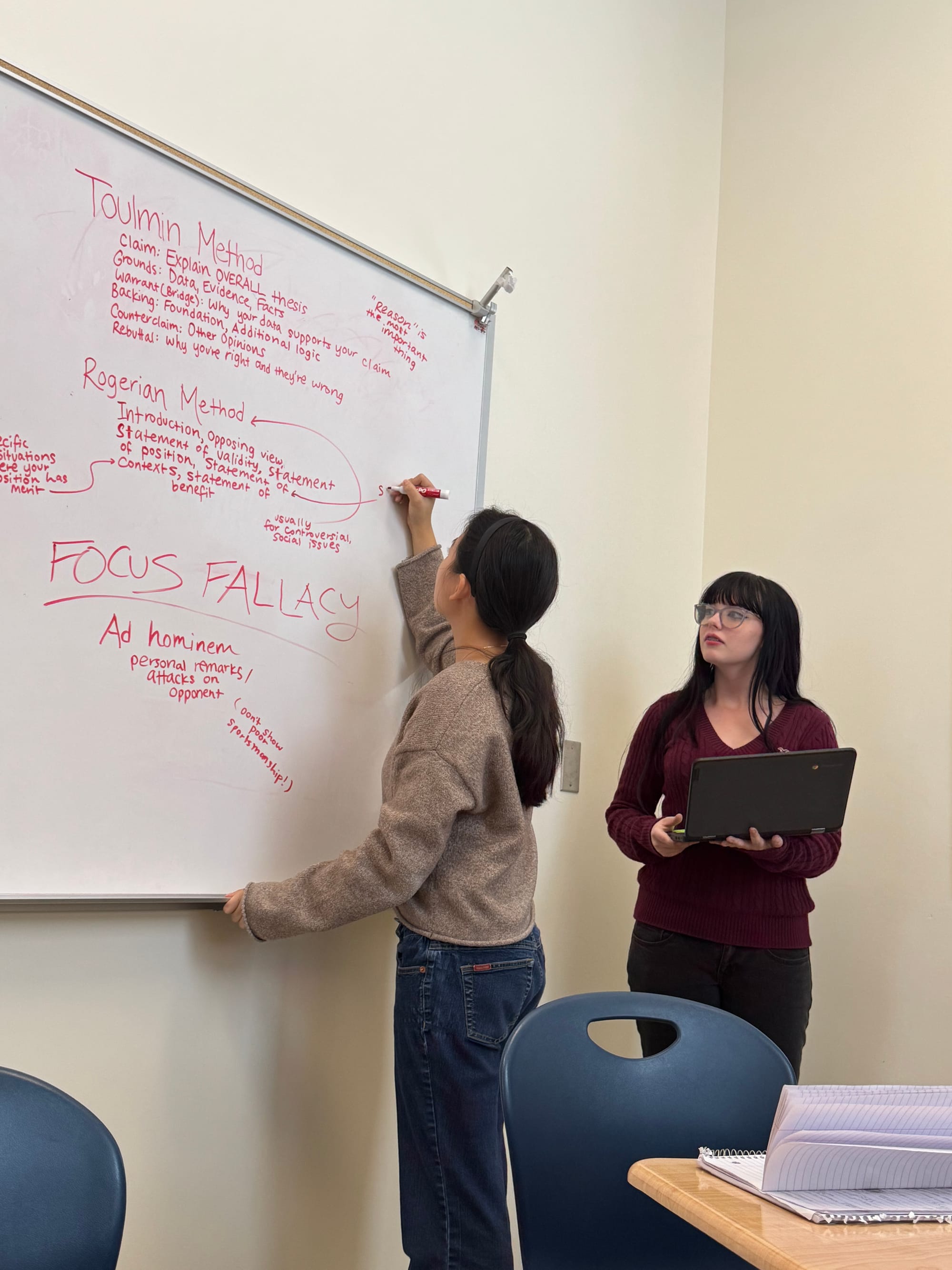 Debate club vice president Evie Jeong, left, and club president Alexus Milligan discuss concepts of argumentation by writing terms on a whiteboard