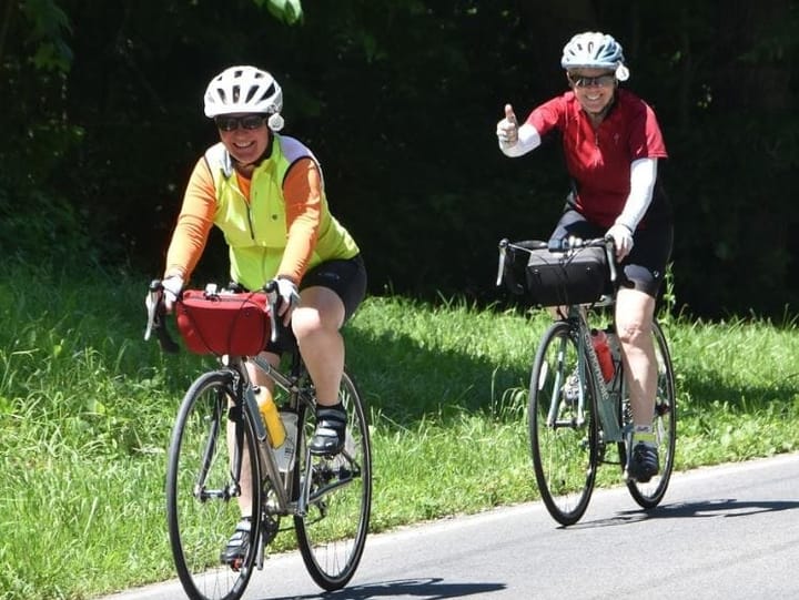 Two cyclists, one in yellow and one in red, ride their bikes along the backroads of Ohio.