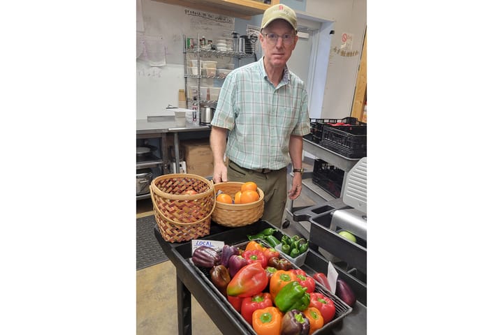 Craig Harkrider stands in a kitchen behind a cart full of green, red, orange and purple peppers