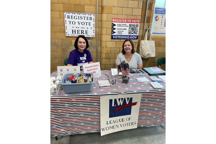 Two women sit behind a LWV table