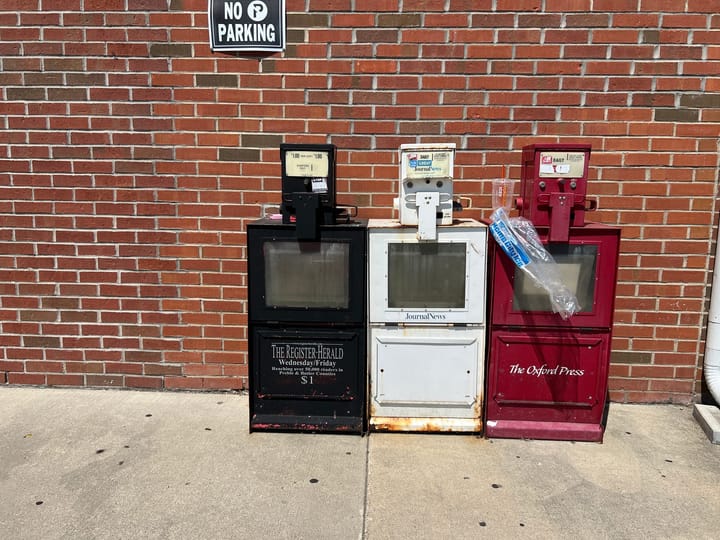 Rusted newstands sit outside a building.
