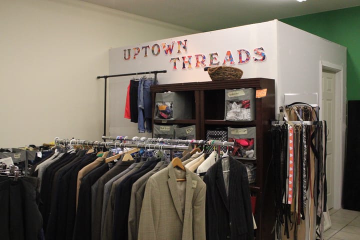 Two clothing racks filled with blazers on hangers sit underneath a sign that reads "Uptown Threads."