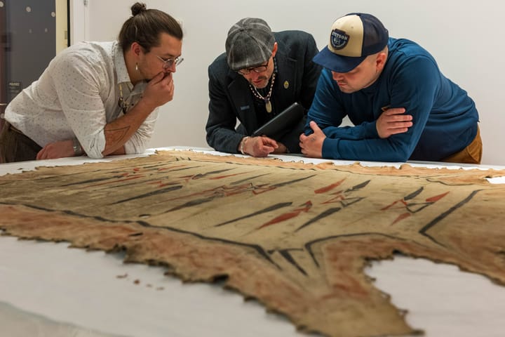 (Left to right) Logan York, George Ironstrack and Nate Poyfair (Miami Tribe of Oklahoma) examine a minosaya, ‘painted hide robe,’ at the exhibit opening at the Palace of Versailles.