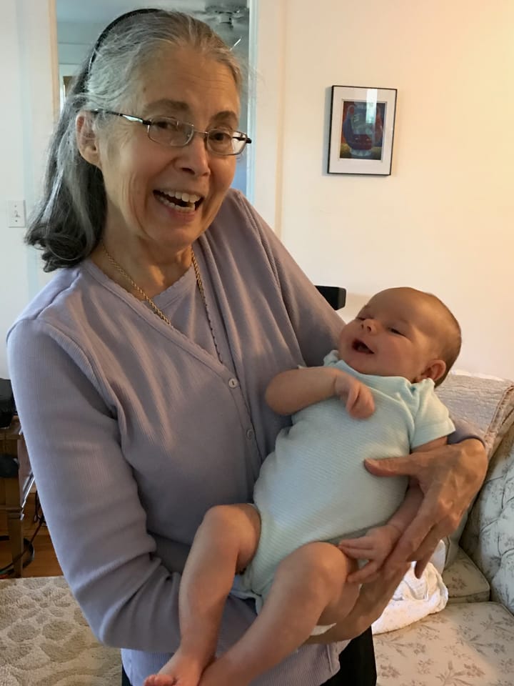 Susan Ann Hershberger, wearing a light purple button up and holding a baby.